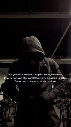 a man wearing a hoodie standing next to some bikes in a building with a quote written on it