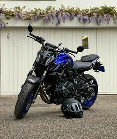 a blue and black motorcycle parked in front of a white building with purple flowers on it