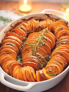 a casserole dish filled with sliced up sweet potatoes and topped with fresh herbs