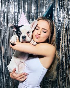 a woman holding a small dog in her arms wearing a party hat and posing for the camera