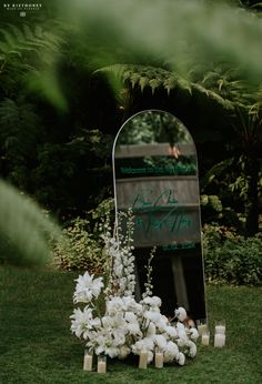 a mirror sitting on top of a lush green field next to flowers and candles in front of it