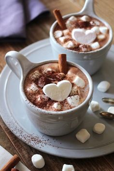 two cups filled with hot chocolate and marshmallows on top of a plate