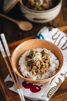 a bowl filled with rice and meat on top of a wooden table next to chopsticks