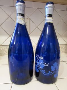 two blue wine bottles sitting on top of a white tile counter next to each other