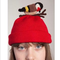 a woman wearing a red beanie with a bird on top of her head in front of a white background