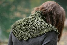 a woman wearing a green knitted shawl and looking down at the ground with trees in the background