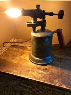 an old coffee grinder sitting on top of a wooden table next to a lamp