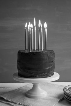 a black and white photo of a birthday cake with lit candles on it, sitting on a table