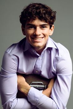 a man in a purple shirt is smiling and holding his arms crossed over his chest