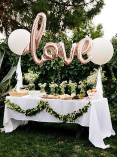 a table topped with balloons and desserts on top of a lush green field next to a love sign