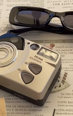 an old camera sitting on top of a table next to some sunglasses and papers with writing