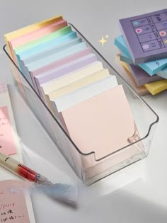 a stack of sticky notes in a clear holder with a pen on the desk next to it