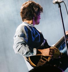 a young man playing an electric guitar in front of a microphone at a music concert