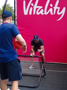 two men in blue shirts and black shorts are playing tennis on a court with a large pink sign behind them