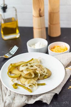 a white plate topped with green beans and onions next to two bottles of olive oil