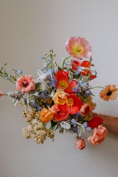 a person holding a bouquet of flowers in front of a white wall with blue, orange and pink flowers