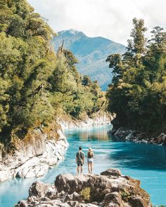 two people standing on the edge of a river