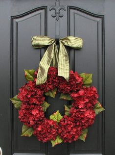 a wreath with red flowers and green leaves is hanging on the front door's black door