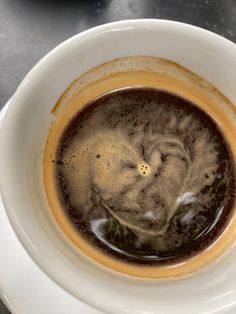 a white bowl filled with liquid on top of a black table next to a cup of coffee