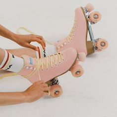 a person wearing pink roller skates tying their laces on the top of one shoe