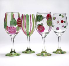 four wine glasses are lined up on a white surface with christmas ornaments painted on them