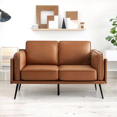 a brown leather couch sitting on top of a hard wood floor next to a potted plant