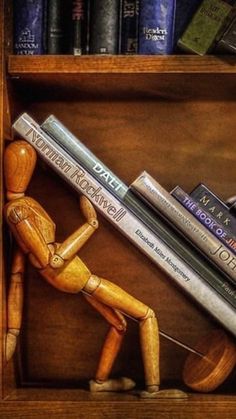 a painting of a wooden man holding two books in front of a book shelf filled with books