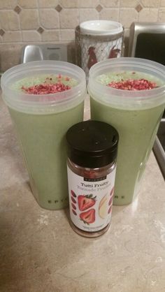 two green smoothies with toppings in plastic cups on a kitchen counter next to a coffee mug