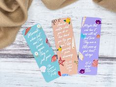 three bookmarks with words on them sitting next to a brown bag and some fabric