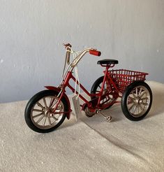 a red toy bike with a basket on the front and back wheels, sitting on a white surface