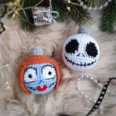 two crocheted pumpkins with faces on them sitting next to christmas tree branches