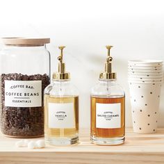 three jars with labels on them sitting on a shelf next to cups and coffee beans