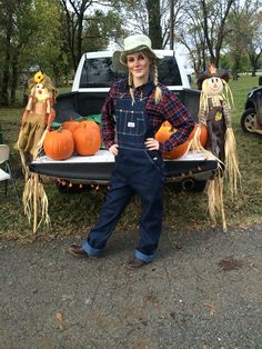 a woman standing in front of a truck with scarecrows and pumpkins on the bed