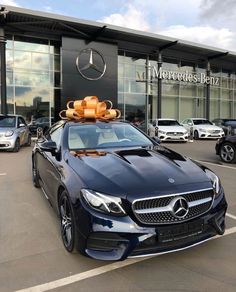 a mercedes benz dealership with cars parked in the parking lot and an orange bow on top