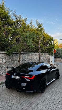 a black sports car parked on the side of a road next to a stone wall