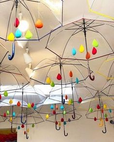 many umbrellas are hanging from the ceiling in an art gallery with colorful drops of rain