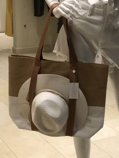 a woman holding a brown and white bag with a hat on it's shoulder