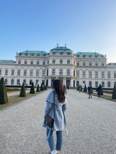 a woman standing in front of a large building with lots of trees and bushes around it