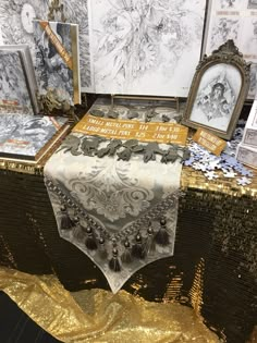 a table topped with pictures and paintings on top of a gold foil covered table cloth