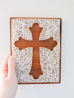 a person holding up a wooden cross with white yarn on the bottom and brown wood