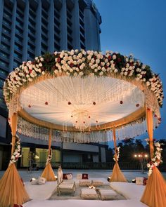 an outdoor wedding setup with white flowers and chandelier on the ceiling, in front of a tall building