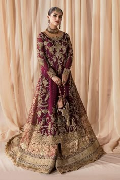 a woman in a maroon and gold bridal gown standing next to a beige curtain