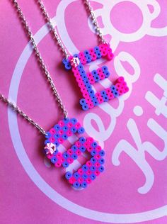 two necklaces made out of lego letters on a pink background