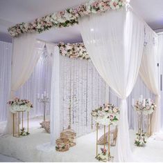 a wedding ceremony setup with white drapes and pink flowers on the wall behind it