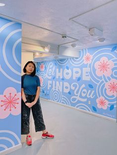 a woman standing in front of a blue wall with pink and white designs on it