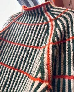 a green and white striped sweater with an orange stripe on the bottom, next to a pair of scissors