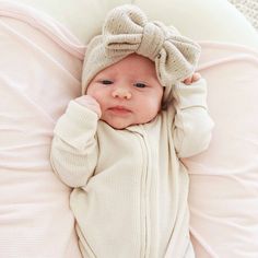 a baby laying on top of a bed wearing a white sweater and a bow headband