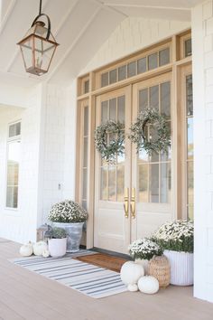 two wreaths on the front porch of a house with white flowers and greenery