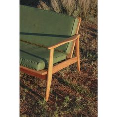 a green couch sitting on top of a grass covered field next to tall dry grass