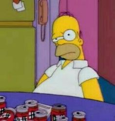 the simpsons is sitting at a table with cans of canned food in front of him